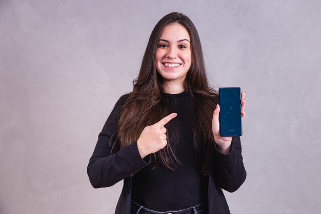 Mujer caucásica apuntando al teléfono celular con espacio para texto sobre fondo gris.