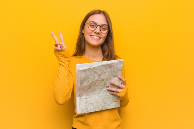 Foto mujer caucásica bonita joven que muestra el número dos, sosteniendo un mapa.