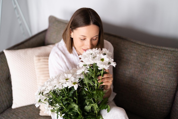 Una mujer caucásica de buen aspecto huele flores y está feliz por recibir un ramo fresco de crisantemo blanco