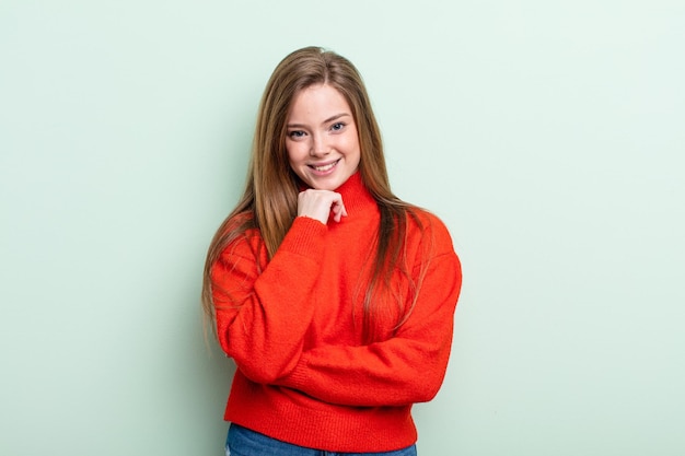 Mujer caucásica de cabello rojo que parece feliz y sonriente con la mano en la barbilla, preguntándose o haciendo una pregunta, comparando opciones