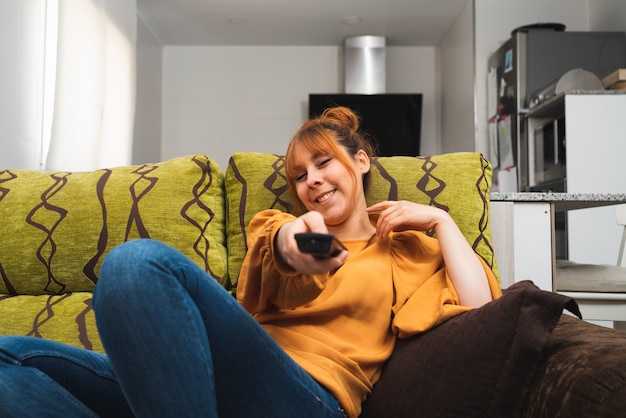 Mujer caucásica cambiando de canal con un mando a distancia sentado en el sofá de casa