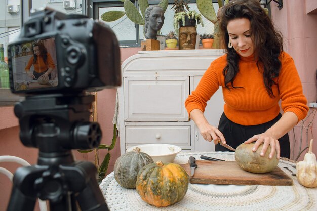 Mujer caucásica en casa haciendo un tutorial de video sobre cómo cortar una calabaza de Halloween