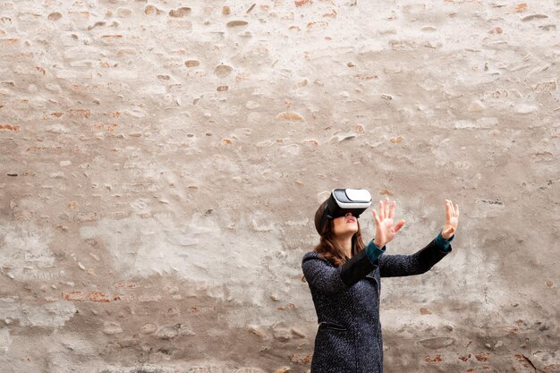 Mujer caucásica con casco de realidad virtual tocando algo. Antiguo muro de fondo con espacio de copia. Concepto de juegos futuristas.