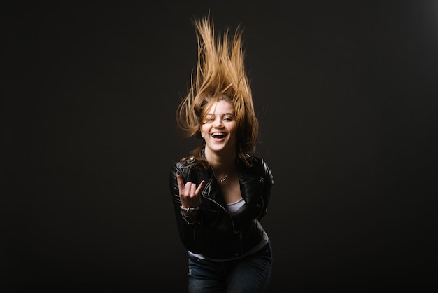 Mujer caucásica con chaqueta de cuero meciendo la cabeza con el movimiento del cabello en el fondo negro