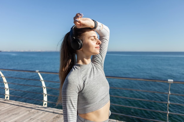 Mujer caucásica delgada escuchando música con auriculares en un día soleado en la playa