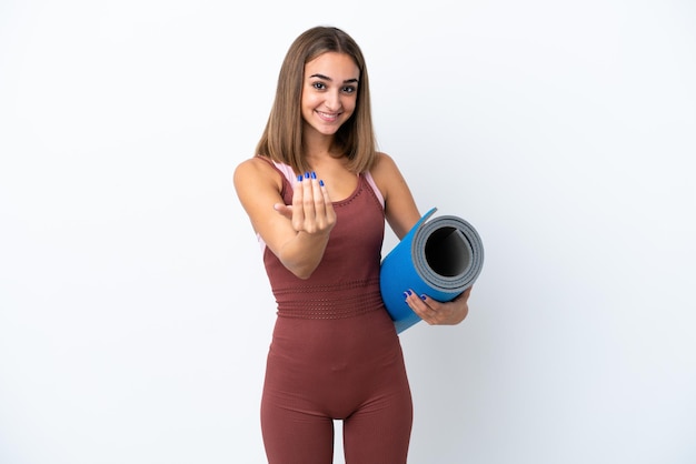 Mujer caucásica de deporte joven que va a clases de yoga aisladas sobre fondo blanco invitando a venir con la mano. Feliz de que hayas venido