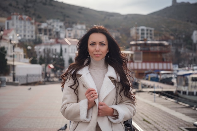 Una mujer caucásica despreocupada en ropa beige disfrutando de la vista del mar en un día cálido y ventoso