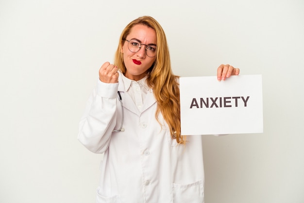 Mujer caucásica del doctor que sostiene un cartel de la ansiedad aislado en el fondo blanco que muestra el puño a la cámara, la expresión facial agresiva.