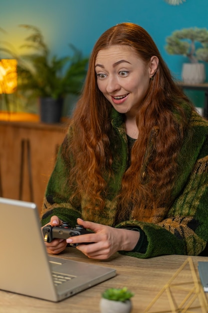 Mujer caucásica emocionada jugando videojuegos en una computadora portátil pasando el tiempo libre en la oficina de casa
