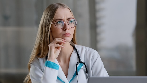 Mujer caucásica enfocada pensativa enfermera practicante médico terapeuta en bata blanca en el hospital