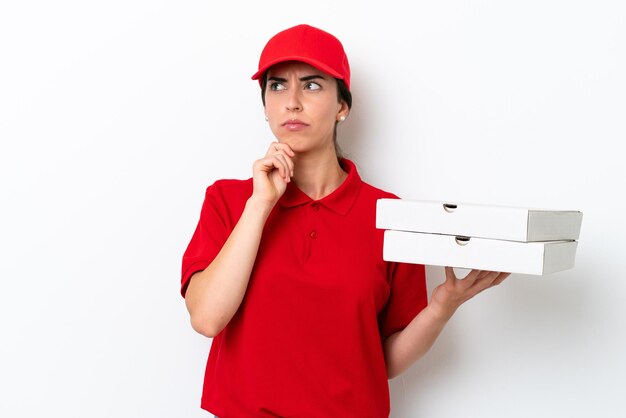 Mujer caucásica de entrega de pizza con uniforme de trabajo recogiendo cajas de pizza aisladas de fondo blanco con dudas y pensando