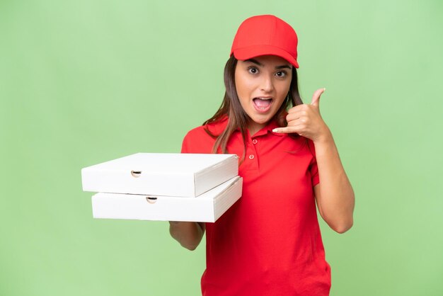 Mujer caucásica de entrega de pizza con uniforme de trabajo recogiendo cajas de pizza aisladas en un fondo de croma verde haciendo gestos telefónicos Llámame de nuevo firmar