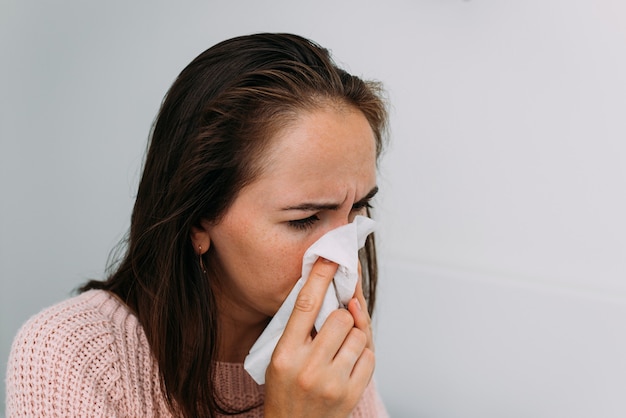 Una mujer caucásica está enferma de un resfriado y se suena la nariz con un pañuelo.