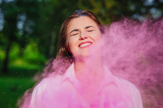 Mujer caucásica expresiva jugando con la explosión de pintura rosa Holi