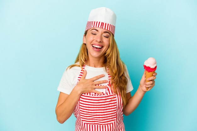 Mujer caucásica fabricante de helado sosteniendo un helado aislado sobre fondo azul se ríe a carcajadas manteniendo la mano en el pecho.