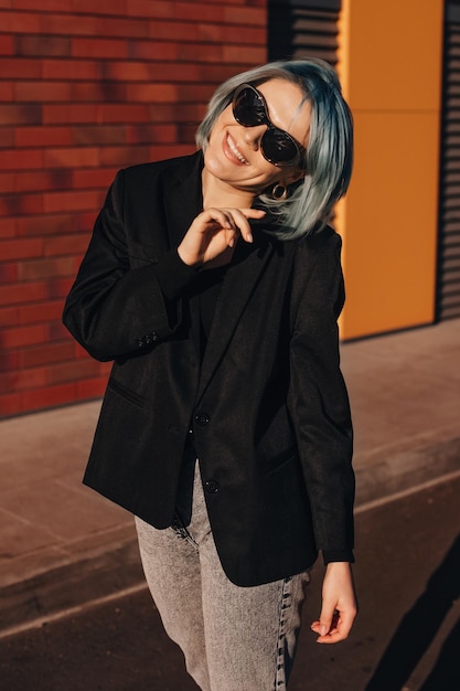 Mujer caucásica en gafas de sol y chaqueta de gran tamaño caminando por la ciudad fash de belleza sonriente con dientes