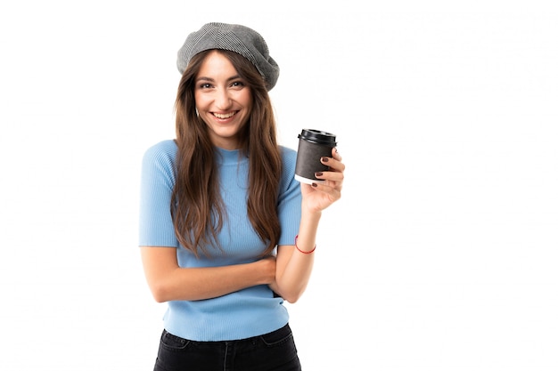 Foto mujer caucásica con gorra bebe café y sonríe, imagen aislada