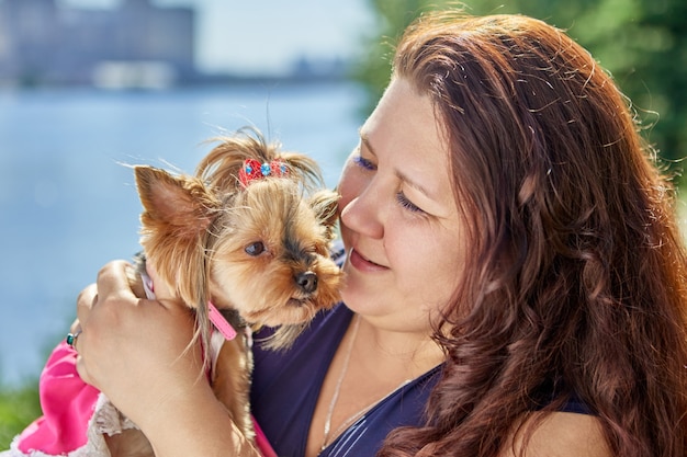 Mujer caucásica de gran complexión sostiene perro yorkshire terrier en sus brazos