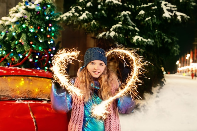 Mujer caucásica en guantes de chaqueta bufanda sombrero haciendo signo amor con bengala por el árbol de navidad