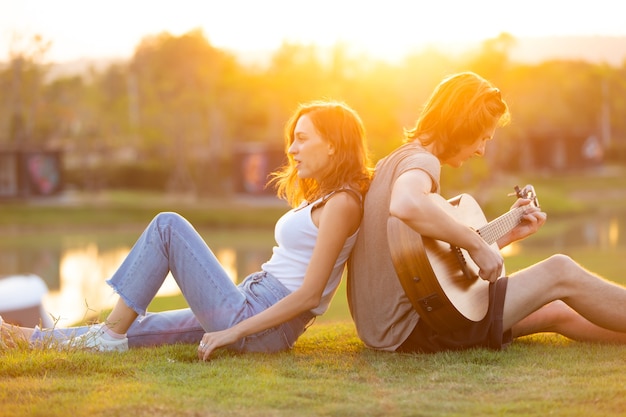 Una mujer caucásica y un hombre guapo pasan tiempo juntos en la naturaleza, acampando y tocando la guitarra.