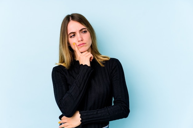 Mujer caucásica joven aislada en azul contemplando, planeando una estrategia, pensando en la forma de un negocio.