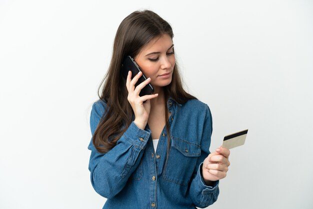 Mujer caucásica joven aislada comprando con el móvil con tarjeta de crédito