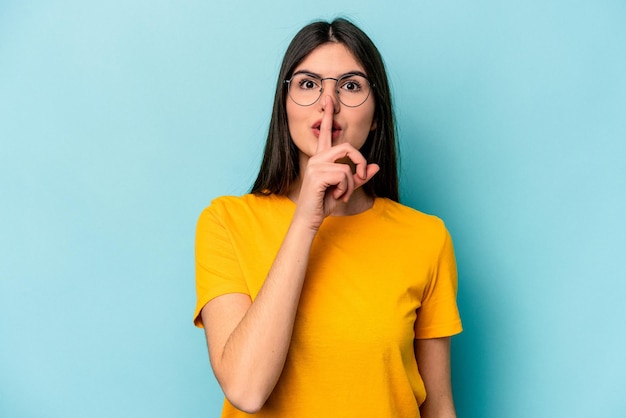 Mujer caucásica joven aislada de fondo azul guardando un secreto o pidiendo silencio