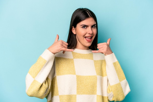 Mujer caucásica joven aislada de fondo azul que muestra un gesto de llamada de teléfono móvil con los dedos