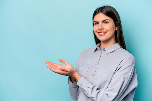 Foto mujer caucásica joven aislada de fondo azul sosteniendo un espacio de copia en una palma