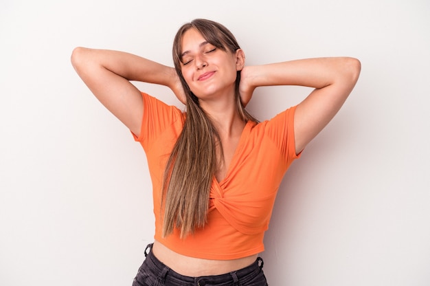 Foto mujer caucásica joven aislada en el fondo blanco que se siente confiada, con las manos detrás de la cabeza.