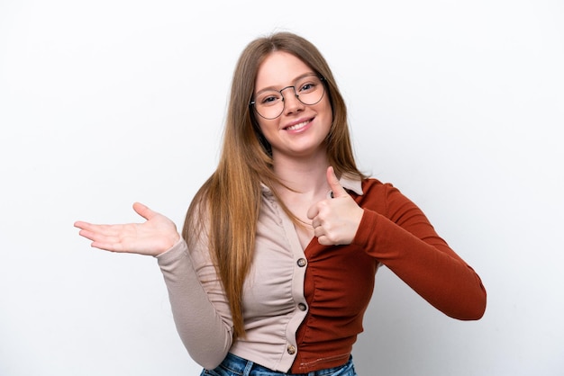 Mujer caucásica joven aislada en fondo blanco sosteniendo copyspace imaginario en la palma para insertar un anuncio y con los pulgares hacia arriba