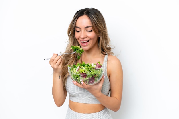 Mujer caucásica joven aislada de fondo blanco sosteniendo un tazón de ensalada con expresión feliz