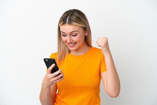 Mujer caucásica joven aislada de fondo blanco usando teléfono móvil y haciendo gesto de victoria