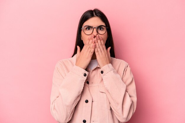 Mujer caucásica joven aislada en un fondo rosado que cubre la boca con las manos preocupadas