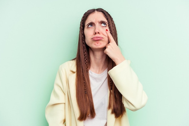 Mujer caucásica joven aislada en un fondo verde llorando, infeliz con algo, concepto de agonía y confusión.