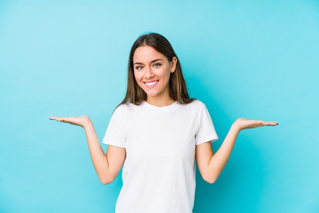 La mujer caucásica joven aislada hace escala con los brazos, se siente feliz y confiada.