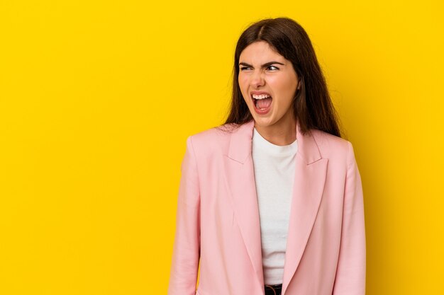 Mujer caucásica joven aislada en la pared amarilla que grita muy enojado, concepto de la rabia, frustrado.