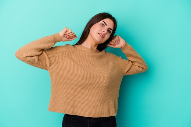 Mujer caucásica joven aislada en la pared azul que estira los brazos, posición relajada.