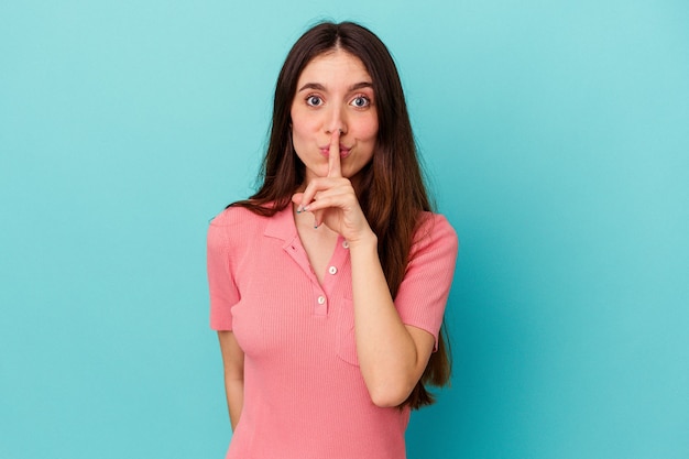 Mujer caucásica joven aislada en la pared azul que guarda un secreto o que pide silencio.