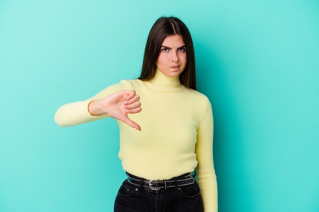 Mujer caucásica joven aislada en la pared azul que muestra el pulgar hacia abajo, concepto de la decepción.