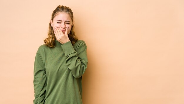 Mujer caucásica joven aislada en la pared beige dudando entre dos opciones.