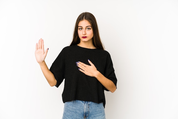 Mujer caucásica joven aislada en la pared blanca que hace un juramento, poniendo la mano en el pecho.