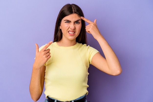 Mujer caucásica joven aislada en la pared púrpura que muestra un gesto de decepción con el dedo índice