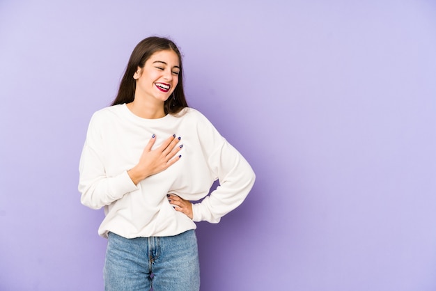 Mujer caucásica joven aislada en la pared púrpura riendo manteniendo las manos en el corazón, concepto de felicidad.