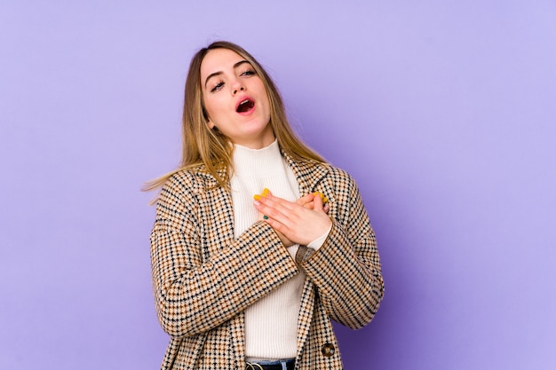 La mujer caucásica joven aislada en la pared púrpura tiene una expresión amistosa, presionando la palma contra el pecho. Concepto de amor.