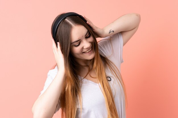 Mujer caucásica joven aislada en la pared rosa escuchando música