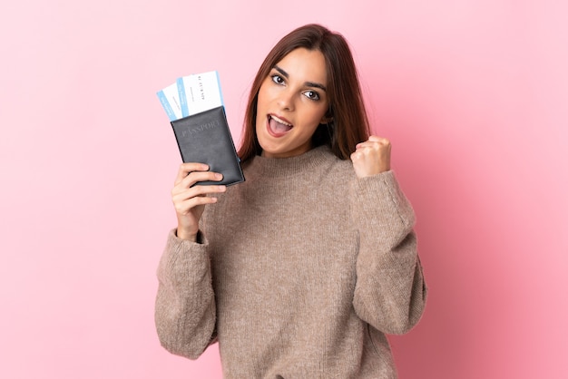 Mujer caucásica joven aislada en la pared rosada feliz en vacaciones con pasaporte y boletos de avión