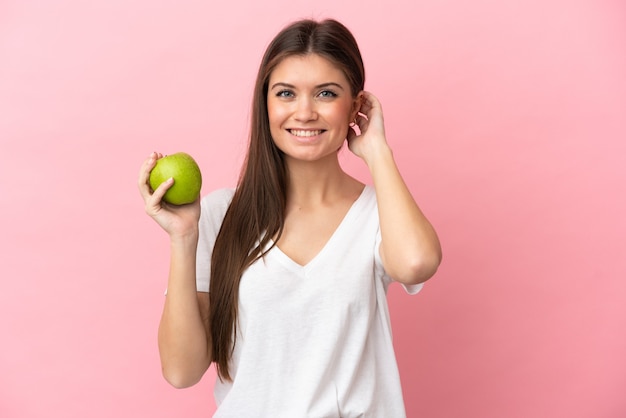 Mujer caucásica joven aislada en la pared rosada con una manzana y feliz