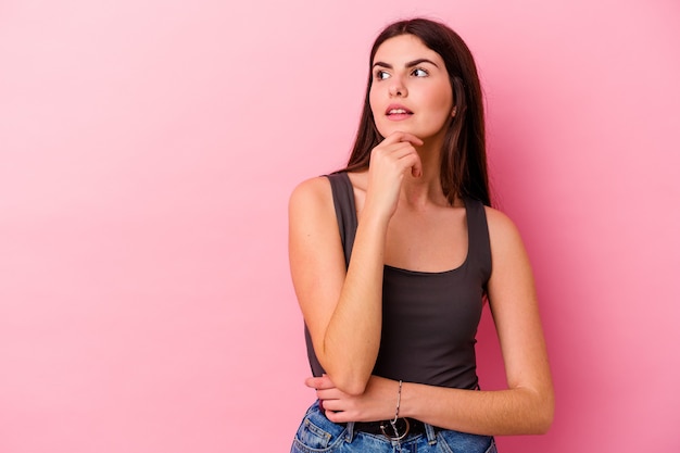 Mujer caucásica joven aislada en la pared rosada relajada pensando en algo mirando un espacio de copia.