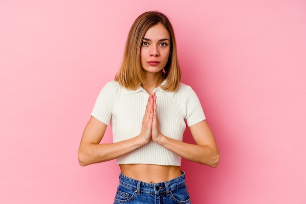 Foto mujer caucásica joven aislada en la pared rosada rezando, mostrando devoción, persona religiosa en busca de inspiración divina.